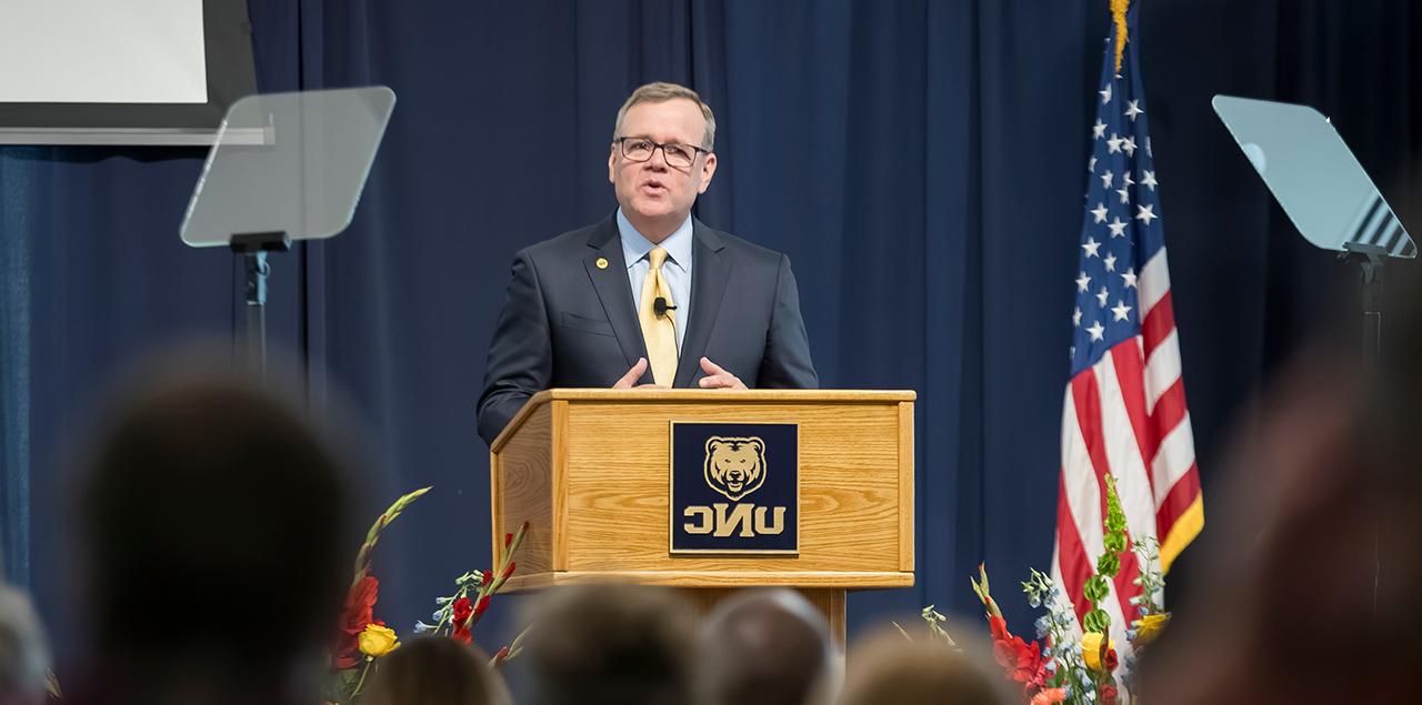 Andy Feinstein standing at a podium on stage addressing a crowd. 